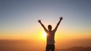 Person standing at sunrise on mountain peak with arms raised in triumph, confident expression, motivational energy, golden hour lighting, natural landscape background