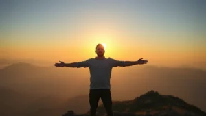 Person standing confidently at mountain summit during golden hour, arms open, sunrise in background, peaceful expression, natural landscape, photorealistic