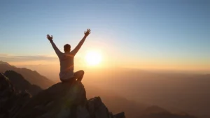 Person sitting on mountain peak at sunrise, arms raised in triumph, vast landscape below, feeling of accomplishment and possibility, golden light, peaceful determination